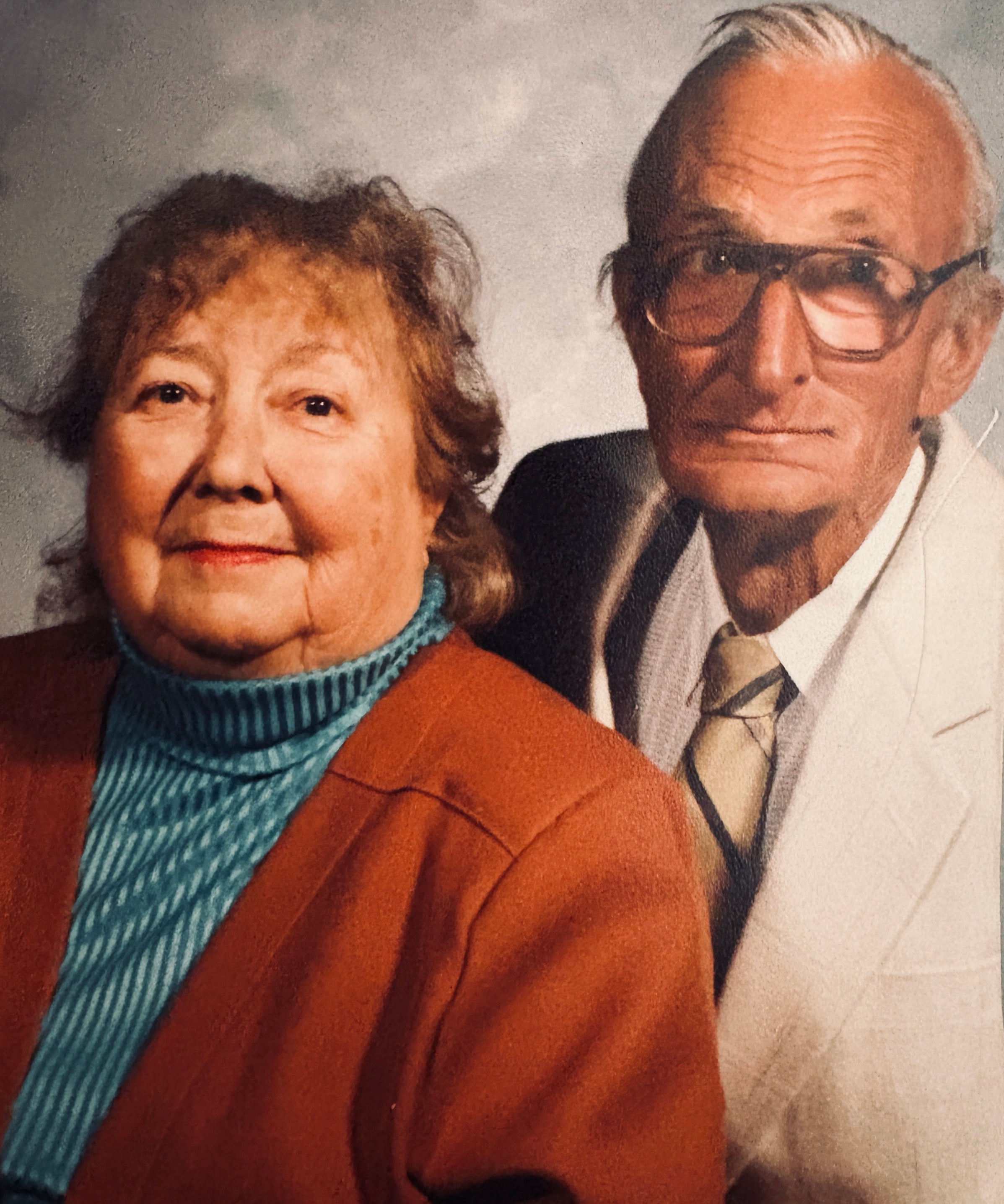 Two elderly people standing side by side against a plain background