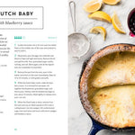 Dutch baby with blueberry sauce on a marble surface with a recipe card.