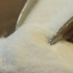 A white powder in a glass bowl with a scoop on a dark background