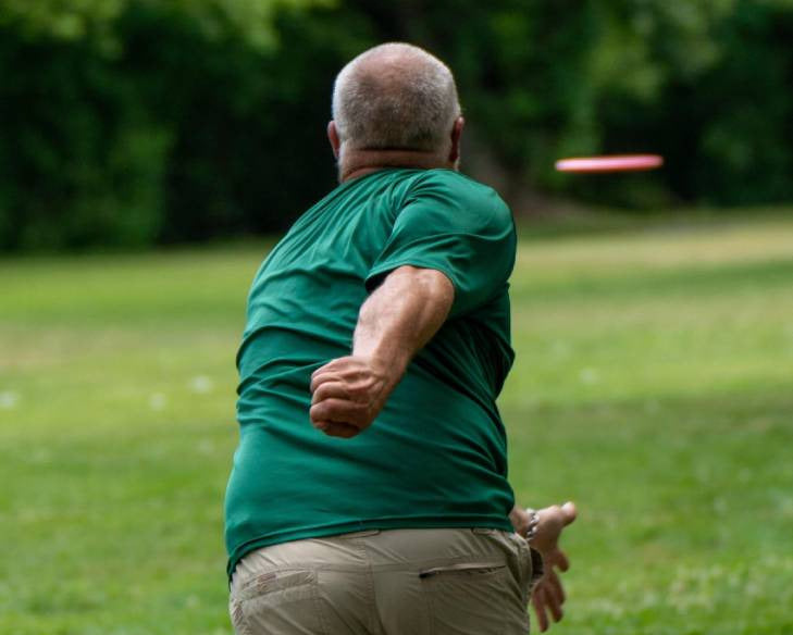 Man in green shirt and beige shorts throwing a disc golf disc in a park.