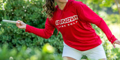 Person in a red Innova Disc Golf shirt playing disc golf in a park.