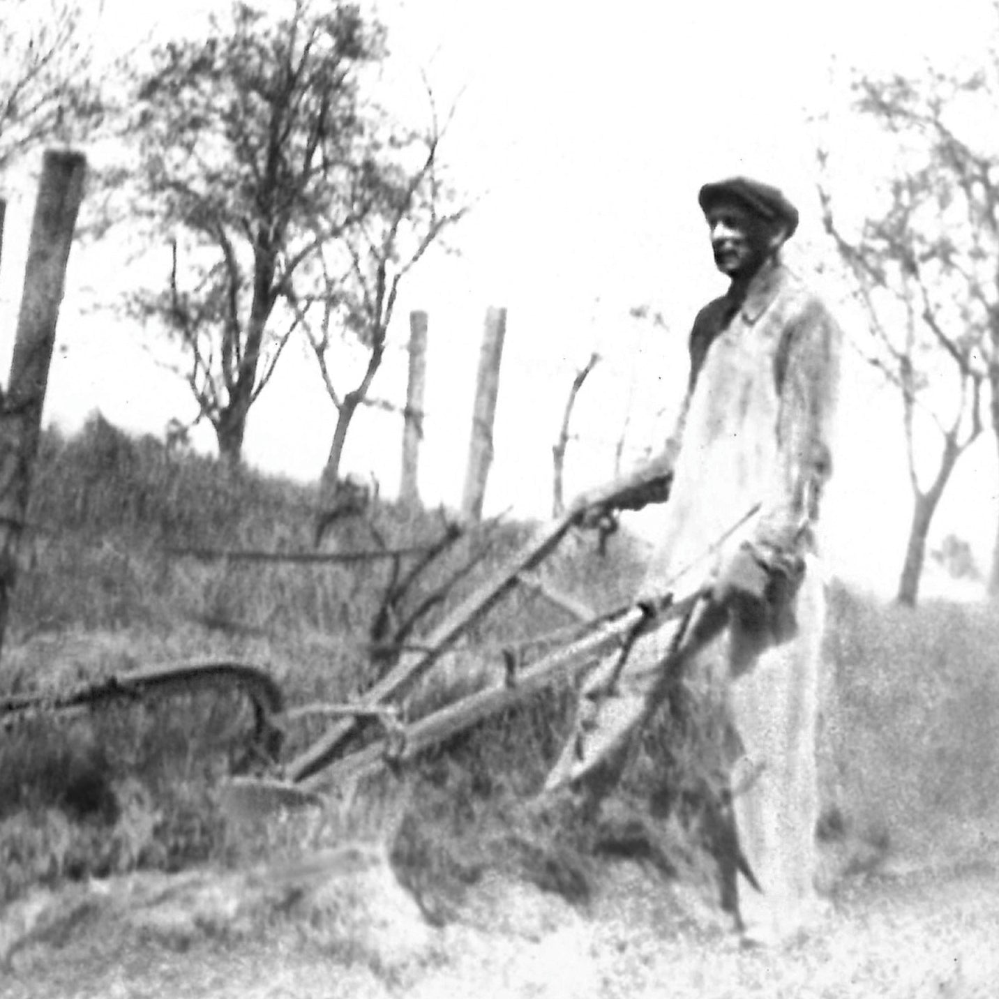 Black and white photograph of a person using a plow in a field with trees in the background