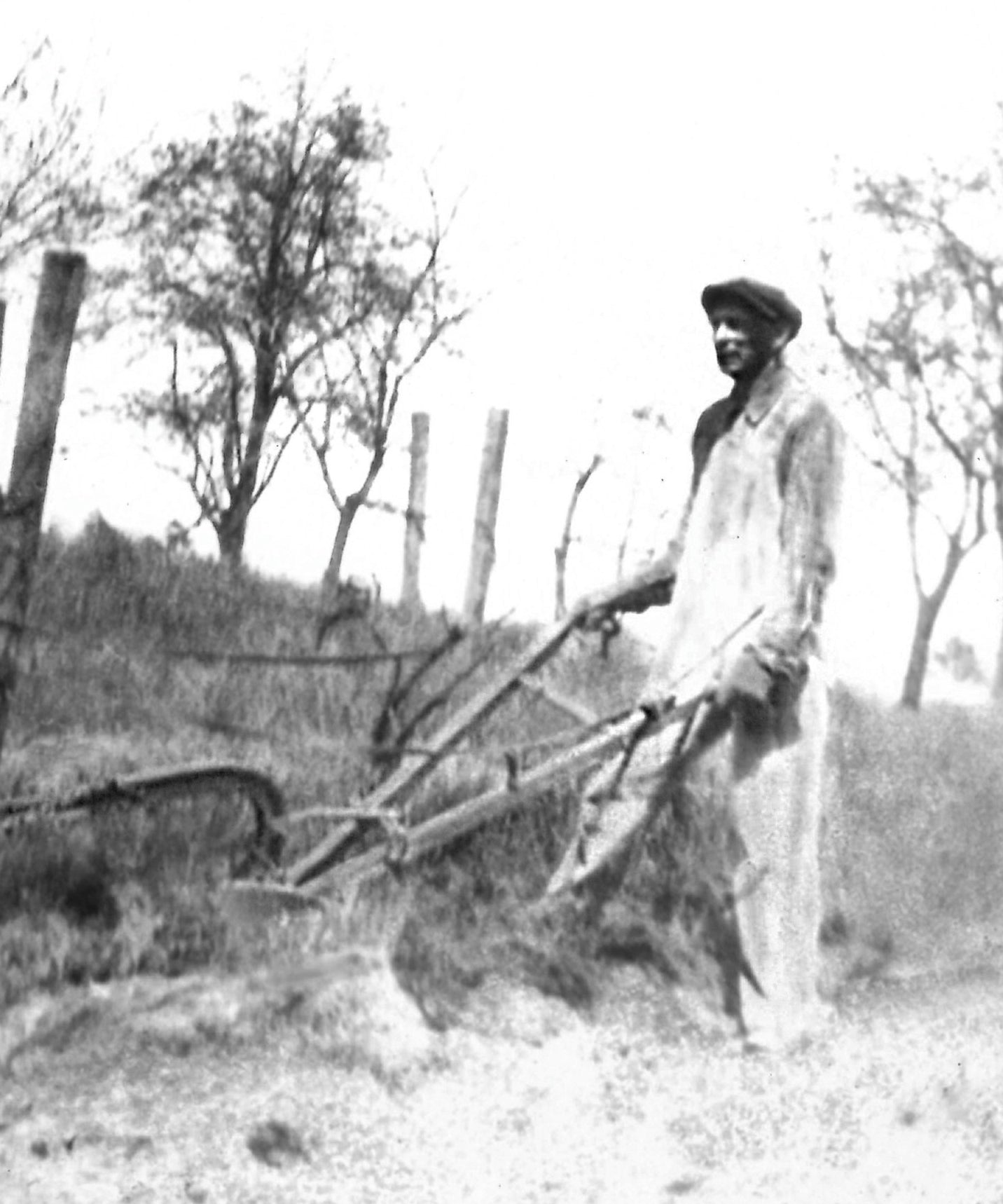 Black and white photograph of a person using a plow in a field with trees in the background