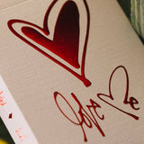 Card with red heart and 'Love' text on a beige background, surrounded by green leaves.