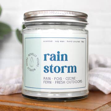 Candle jar labeled 'rain storm' on a wooden surface with a light background