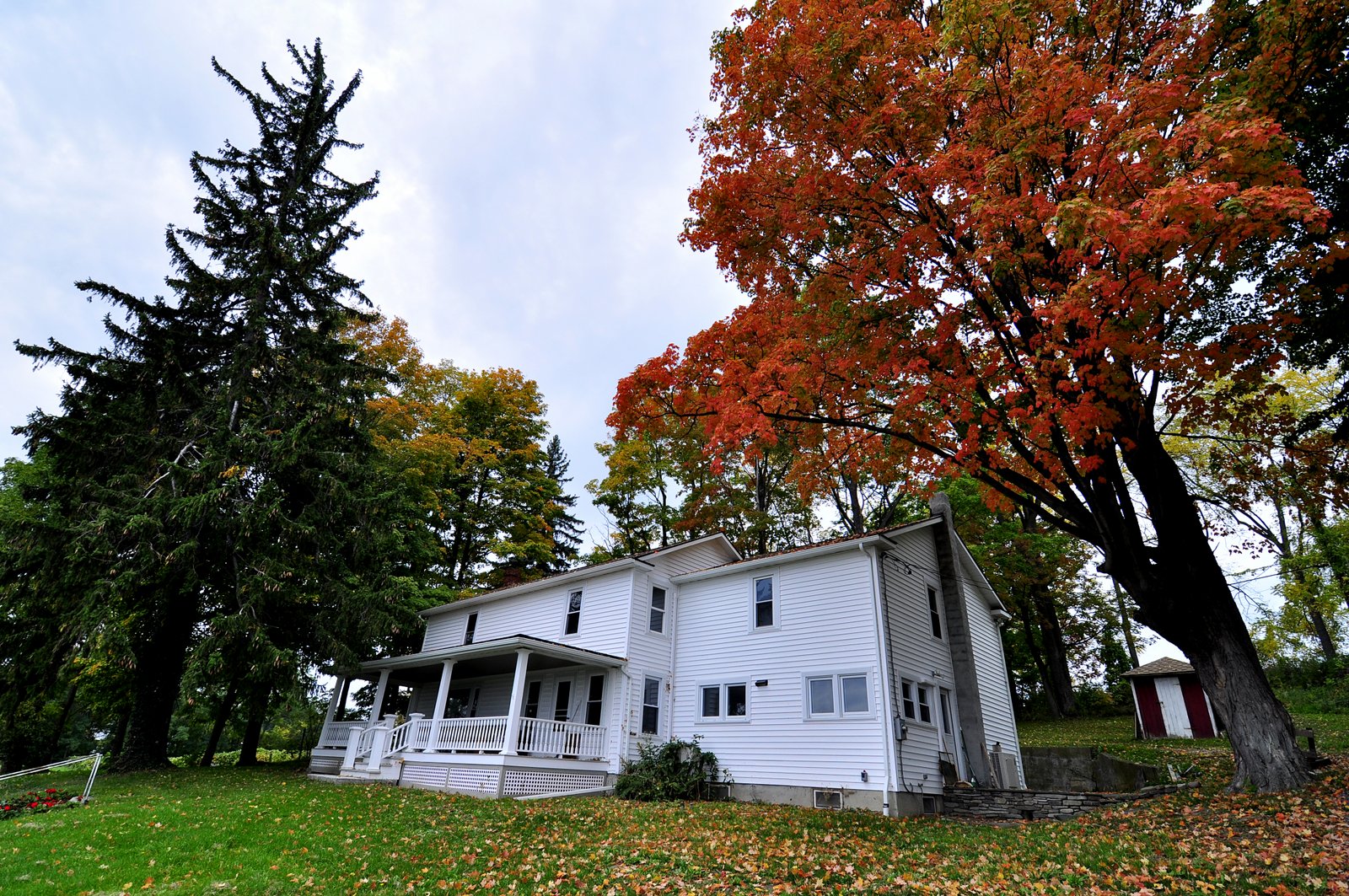 White house with a porch surrounded by trees with autumn foliage.