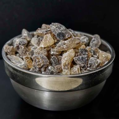 Metal bowl filled with raw sugar chunks on a black background