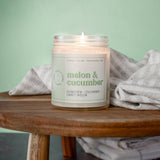 Candle labeled 'Melon & Cucumber' on a wooden surface with a light green background