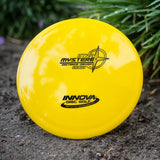 Yellow disc golf disc with 'Innova Disc Golf' branding on a natural background